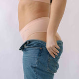 Woman putting on a pair of jeans  wearing the Ada ribbed seamless high waisted knicker from Six. Suitable to wear throughout pregnancy, maternity and as a supportive post C section knicker.