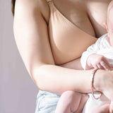 Woman sat breastfeeding her baby wearing the Ada ribbed seamless nursing bra from six in the blush nude colour.