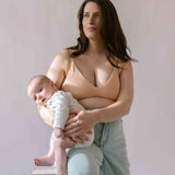 Woman sat holding her baby wearing the Six Ada seamless ribbed nursing bra in Nude Blush colourway. Comfortable and supportive nursing bra to be worn through pregnancy and breastfeeding.