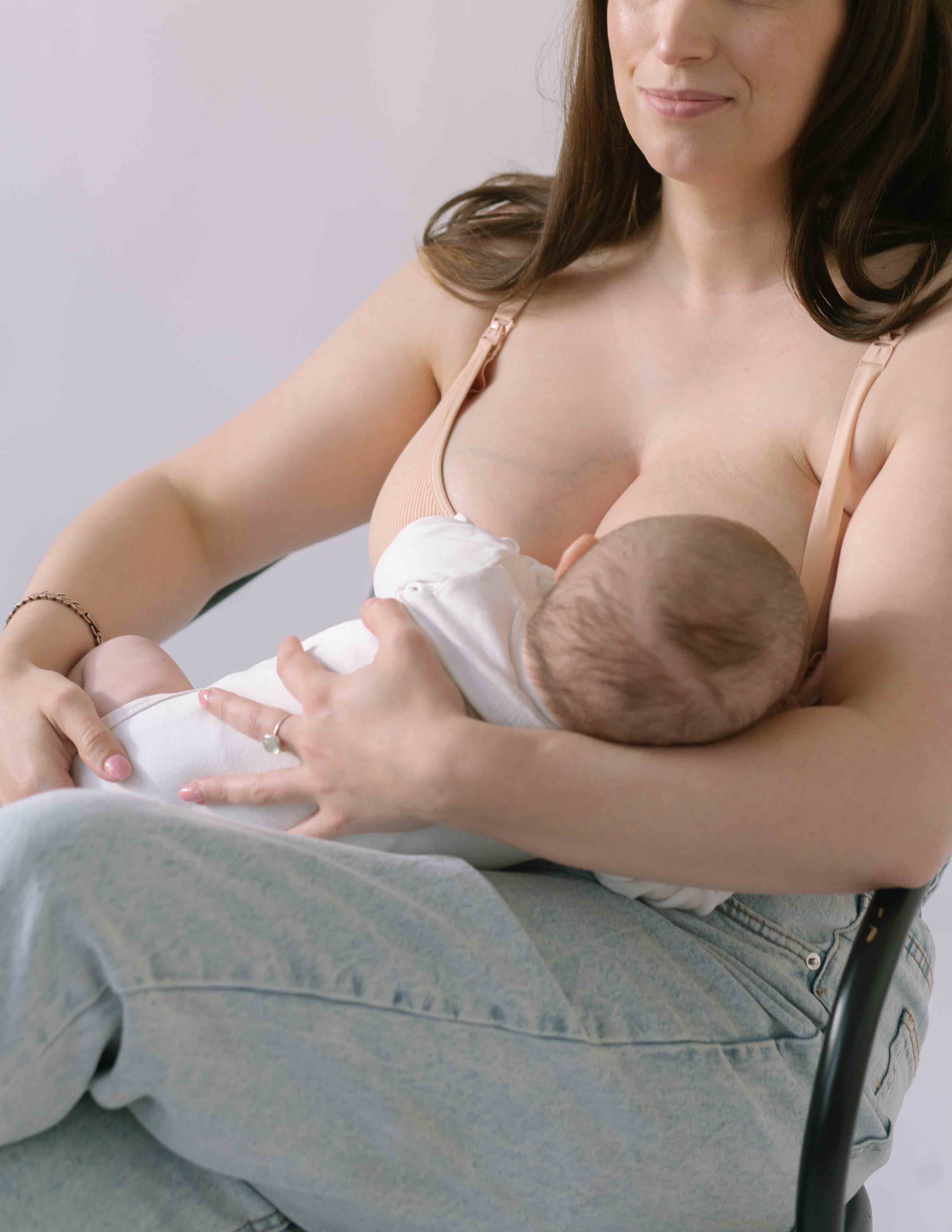 Woman sat breastfeeding her baby wearing the Ada ribbed seamless nursing bra from six in the blush nude colour.